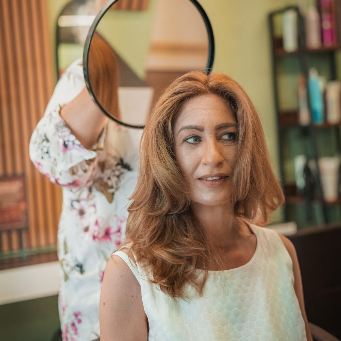 Frau in modischer Kleidung steht vor einer weißen Wand mit Fenstern und einer Tür.